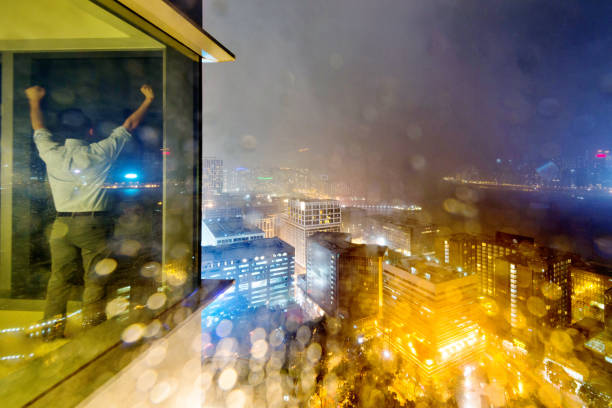 Businessman standing by the window with arms raised at night.