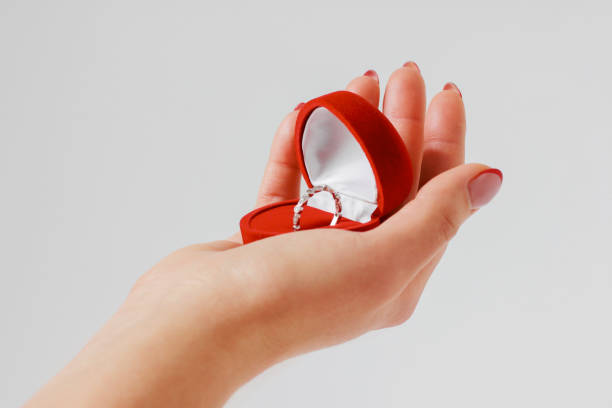 istock Woman hand with engagement ring in red box on gray background is 1071977620