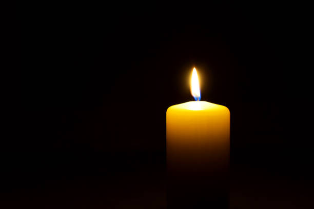 One yellow candle flame  burning in darkness One yellow candle flame  burning in darkness on black background with copy space for text. candle stock pictures, royalty-free photos & images