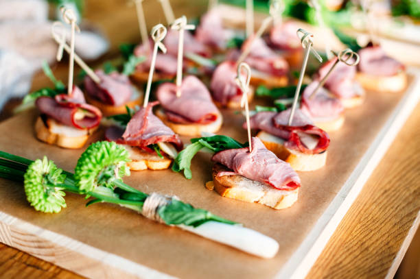 istock Delicious catering banquet buffet table decorated in rustic style in the garden. Different snacks, sandwiches with ham and greenery on a wooden plate. Outdoor. 1072005134