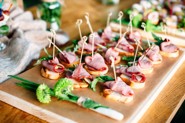 istock Delicious catering banquet buffet table decorated in rustic style in the garden. Different snacks, sandwiches with ham and greenery on a wooden plate. Outdoor. 1072005142