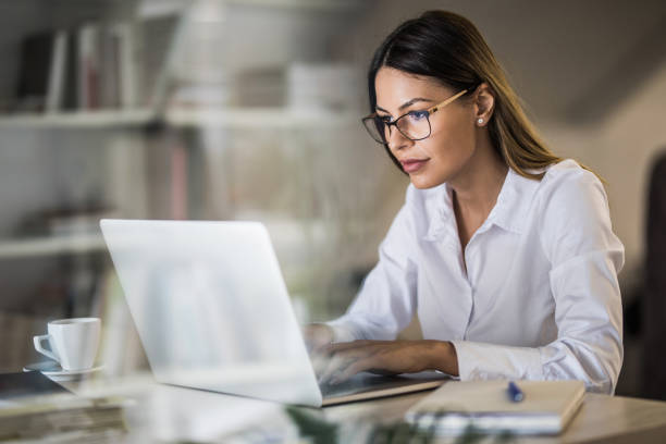 młoda bizneswoman wpisując e-mail na laptopie w domowym biurze. - biała kobieta czyta w okularach zdjęcia i obrazy z banku zdjęć
