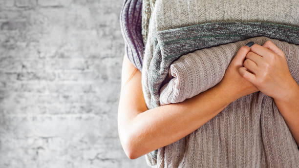 woman holding in hands Stack of cozy knitted sweaters on gray wall background