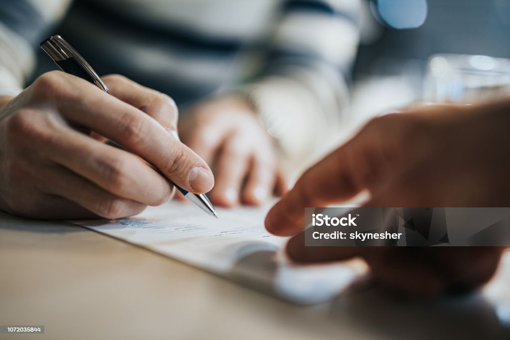 Sign here please! Close up of unrecognizable man signing a contract while financial advisor is aiming at the place he need to sign. Contract Stock Photo