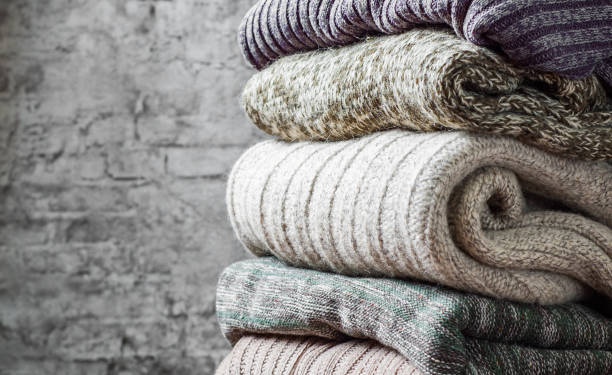 Stack of cozy knitted sweaters on gray wall background Stack of cozy knitted sweaters on gray wall background blanket stock pictures, royalty-free photos & images