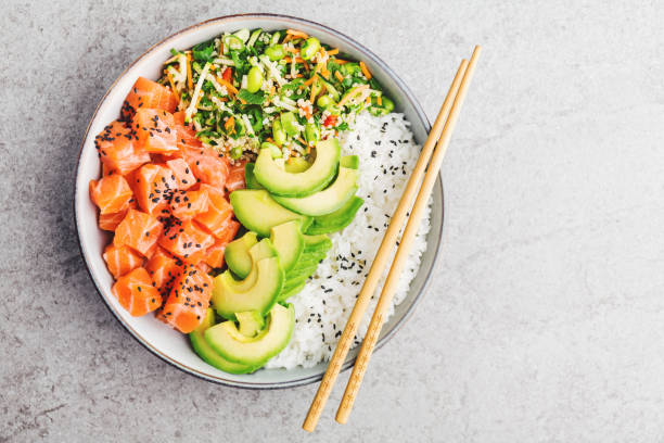 Poke bowl with salmon served in bowl Tasty appetizing poke bowl served with salmon, avocado, rice, salad with edamame. Grey background. View from above with copy space. fish in a bowl stock pictures, royalty-free photos & images