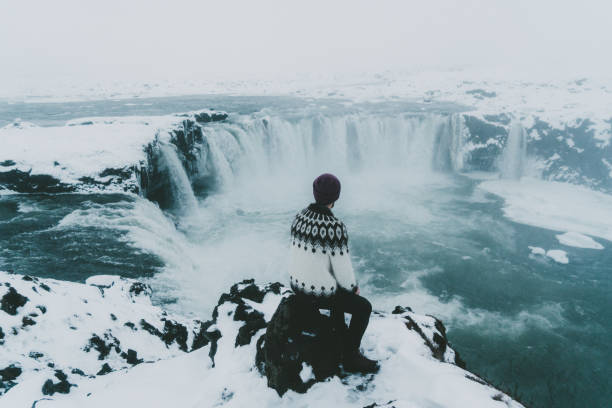 Young Caucasian man in Icelandic sweater  looking at scenic view of waterfall in winter