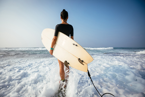 Woman surfer with surfboard walking on mossy seashore reefs