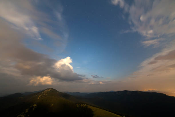 istock Summer night in mountains. Starry dark blue sky and white clouds at sunset over mountain range. 1072060768