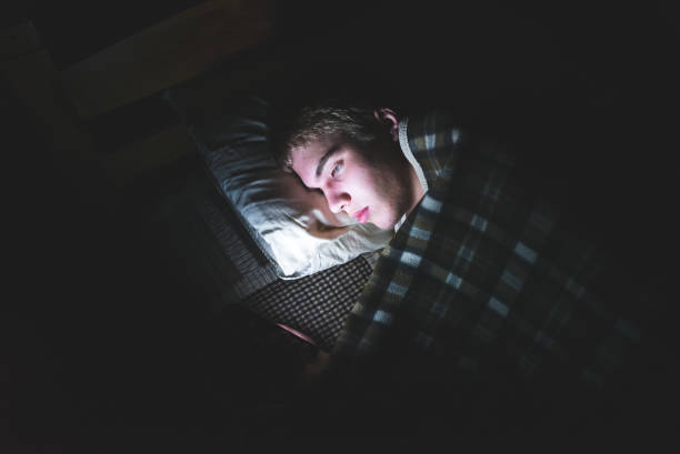 Depressed teenager on his phone in the dark. stock photo