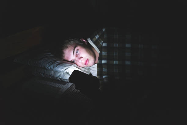 Depressed teenager on his phone in the dark. stock photo