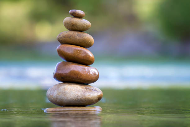 istock Close-up abstract image of wet rough natural brown uneven different sizes and forms stones balanced like pyramid pile landmark in shallow water on blurred blue-green misty copy space background. 1072077248