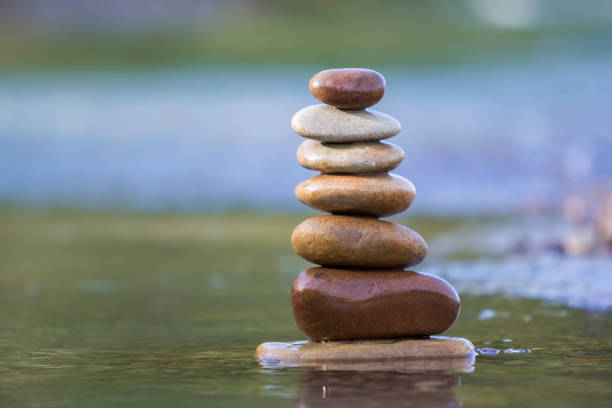 istock Close-up abstract image of wet rough natural brown uneven different sizes and forms stones balanced like pyramid pile landmark in shallow water on blurred blue-green misty copy space background. 1072077324
