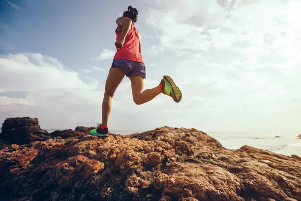 Photo of Young fitness woman trail runner running to rocky mountain top on seaside