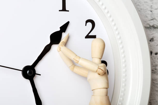 Wooden human figure trying to stop the arrow of the clock. Ageing concept stock photo
