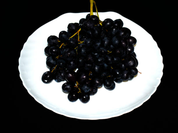 istock Black ripe grapes on a white plate. White plate on black background. 1072123286