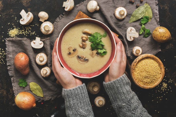 las mujeres las manos en un suéter gris sosteniendo un tazón de sopa crema de champiñones. sopa de invierno caliente sobre un oscuro fondo rústico. vista superior, completamente laica. - healthy eating food vegetable fungus fotografías e imágenes de stock