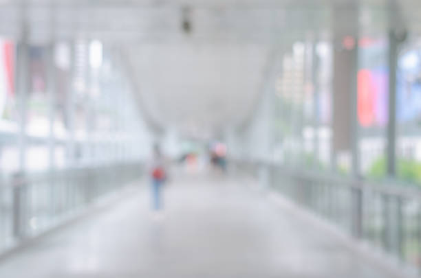 A bridge with a pedestrian walking in the center. The backlit scene creates a striking silhouette effect for both the pedestrian and the bridge's wave-like railing. The blue sky and white clouds in the background provide a beautiful contrast to the dark silhouettes.