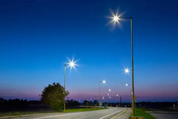 Photo of night empty road with modern LED street lights, entrance to a small town
