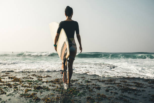 istock Woman surfer with surfboard walking on mossy seashore 1072173798