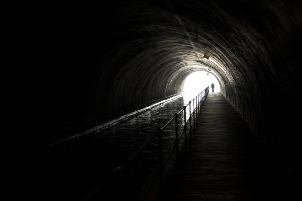 silhouette di un uomo appraching di fronte alla luce intensa alla fine di un tunnel buio - spirituality light tunnel light at the end of the tunnel foto e immagini stock