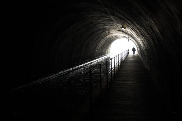 silhouette d’un homme de appraching devant une lumière intense à la fin d’un tunnel sombre - spirituality light tunnel light at the end of the tunnel photos et images de collection