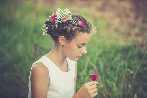 teenage girl picking a rose while wearing a floral wreath in nature environment.