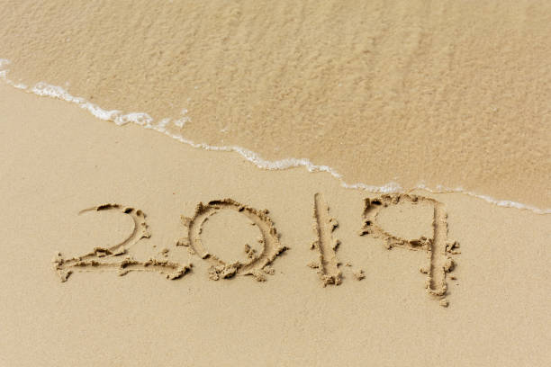 istock Number 2019 written on sand beach with waves 1072178960