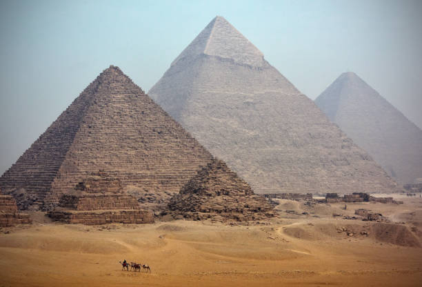 Homeward bound A distant camel caravan passes the majestic pyramids at Giza in Cairo at dusk. Egypt homeward stock pictures, royalty-free photos & images