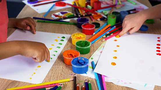 Children putting colorful dots on paper with fingers, painting a picture