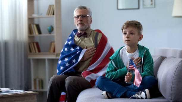 Patriotic old man holding American flag, listening national anthem with grandson Patriotic old man holding American flag, listening national anthem with grandson national anthem stock pictures, royalty-free photos & images