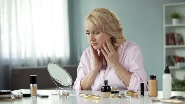 Sad pretty lady looking in mirror, touching her face, anti-wrinkle skin care