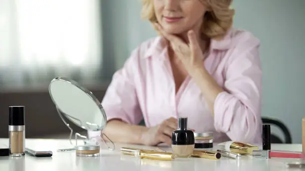 Anti-aging make-up products with mature lady looking in mirror behind, beauty