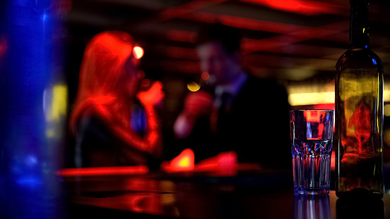 Man and woman dating in nightclub, both drinking beverages, blurred background