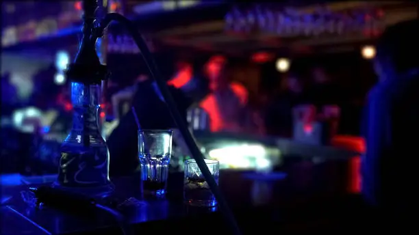 Photo of Hookah and two glasses standing on bar counter at night club, party atmosphere