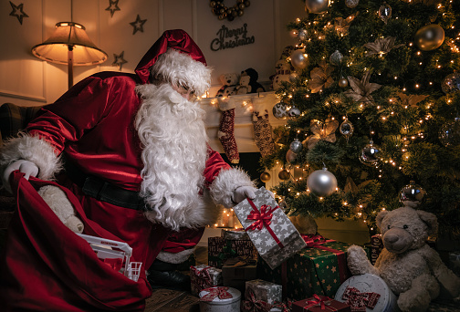 Santa Claus putting gifts under the christmas tree at night