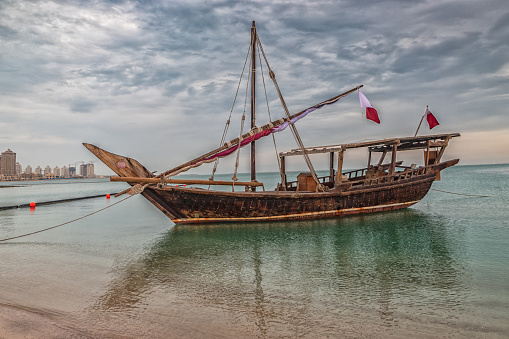 Traditional wooden boat dhow in Katara beach Qatar with clouds and skyline in background