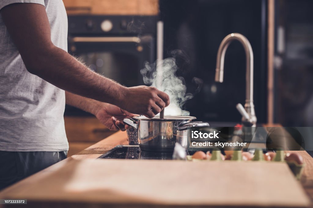 Unrecognizable man making lunch in the kitchen and stirring soup. Unrecognizable man stirring soup in a saucepan while making lunch in the kitchen. Cooking Stock Photo