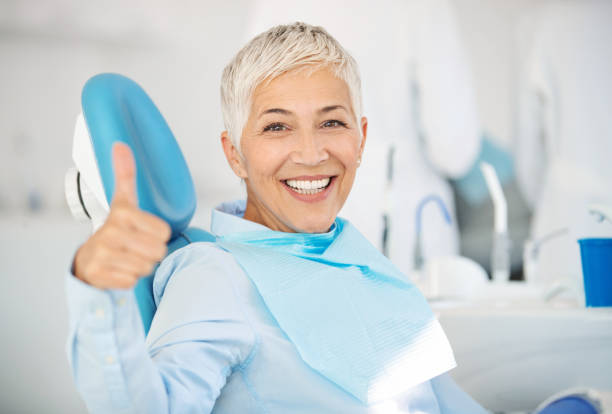 Successful dentist appointment. Closeup front view of a cheerful mid 50's female patient happily smiling to the camera and showing thumbs up after successful dental procedure. dental cavity photos stock pictures, royalty-free photos & images
