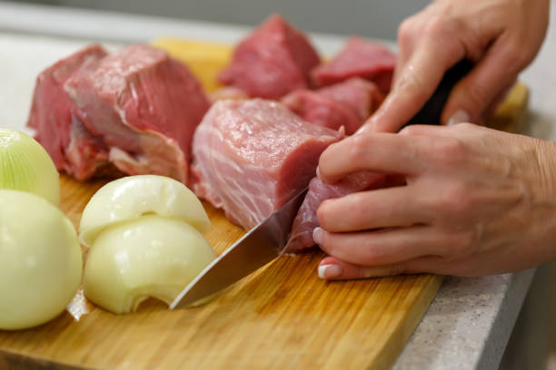 istock Cook cuts raw meat in large pieces on a wooden board 1072236196