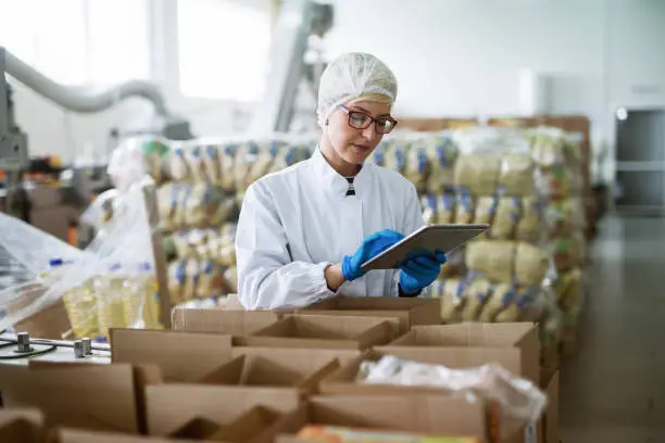 Photo of Female worker using tablet for checking boxes while standing in food factory.