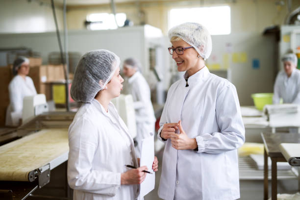 istock Two female workers discussing while standing in food factory. 1072244334