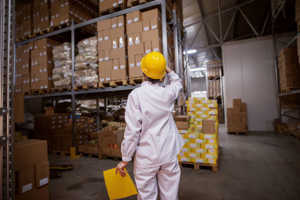 istock Female worker looking up while holding with one hand helmet and in other hand holding folder with paperwork. Storage interior. Backs turned. 1072245348
