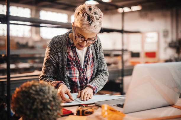 istock Woman doing paperwork while standing in carpenter workshop. Female doing male's work concept. 1072253076