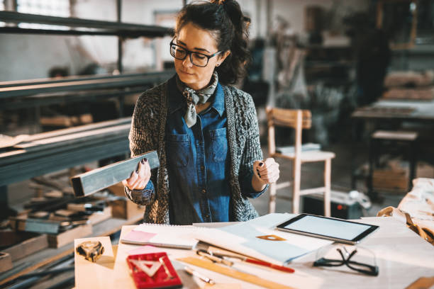 istock Female carpenter working in workshop. On desk rulers, paperwork and tablet. 1072254628