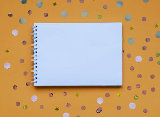 istock White writing pad on orange background with confetti. 1072287800