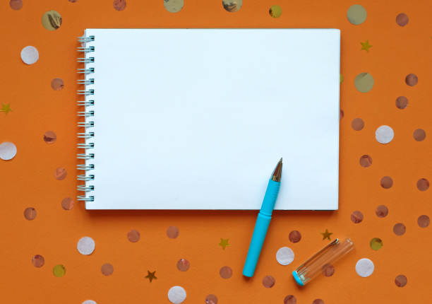 istock White writing pad on orange background with confetti. 1072287804