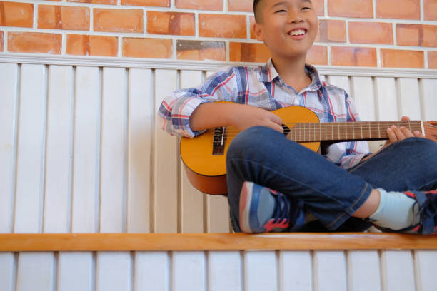 istock asian kid boy child playing guitar ukulele. children leisure activity 1072287970