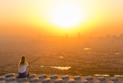 Adventurous woman sitting on top of skyscraper overlooking the city at sunrise