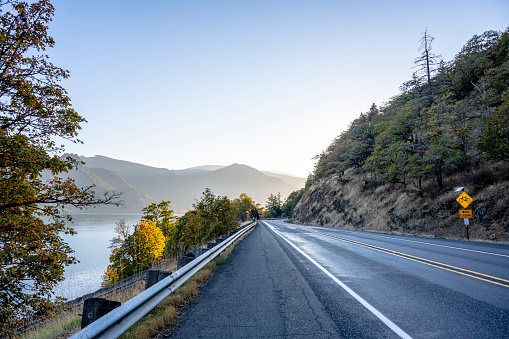 Autumn landscape a highway along the Columbia River with a restrictive belt for drift safety and a river on one side and a rocky mountain covered with trees on the other side abuts the horizon